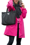 A person is wearing an iconic looselyboho BARBARA PINK WINDBREAKER OUTFIT, black scarf, and black pants. They are holding the handle of a black tote bag with a white "GW" logo printed on it. The person is partially showing their face and has gray hair. The background is white.