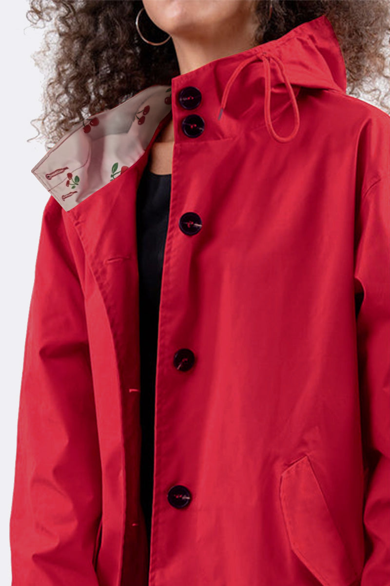 A person wearing The WJacket's Water Resistant Oversized Hooded Windbreaker Rain Jacket in a vibrant red, complete with a unique cherry-patterned inner lining, exudes timeless style. This stunning coat showcases rare and beautiful colors and features a hood, allowing part of the person's curly hair and hoop earring to be visible against a plain light-colored background.