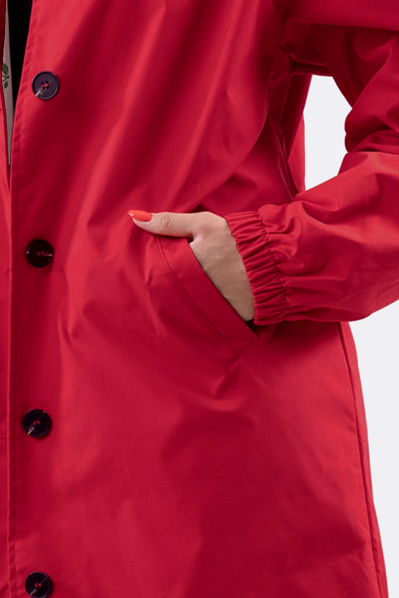 Close-up of a person wearing The WJacket's Water Resistant Oversized Hooded Windbreaker Rain Jacket in bright red, featuring black buttons. The left hand is partially inserted into one of the jacket's pockets. The sleeve is elastic at the wrist, and the person's nails are painted orange. This ensemble showcases timeless style and rare beautiful colors.