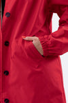 Close-up of a person wearing The WJacket's Water Resistant Oversized Hooded Windbreaker Rain Jacket in bright red, featuring black buttons. The left hand is partially inserted into one of the jacket's pockets. The sleeve is elastic at the wrist, and the person's nails are painted orange. This ensemble showcases timeless style and rare beautiful colors.