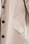 Close-up of a beige trench coat showing the side pocket and four black buttons. The fabric appears smooth and slightly shiny, suggesting it's a stylish BISCUIT BEIGE WINDBREAKER crafted from lightweight water-resistant material by looselyboho.