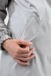 Close-up of a person wearing a looselyboho ICE GRAY WINDBREAKER. The person’s right hand is partially inside a side pocket of the coat, with thumb outside and other fingers inside the pocket. The coat sleeve features a cinched cuff.